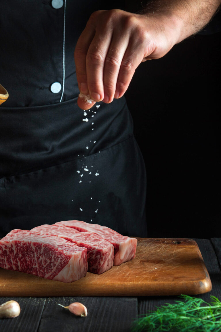 steak being seasoned on a wooden cutting board